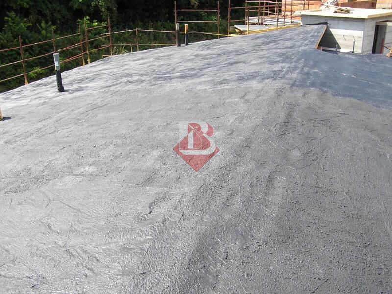 Vista ravvicinata di un tetto impermeabilizzato con una membrana grigia, applicata su una superficie piana con barriere di sicurezza arancioni in lontananza.